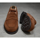 A brown suede penny loafer with a Dainite rubber sole, showing a classic round toe shape and a signature penny slot detail & Dainite Soles