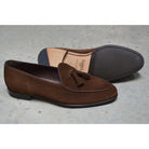 A dark brown suede tassel loafer with a Vegano Moka leather trim, displaying an almond-shaped toe and a fine ridged rubber sole.