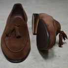 A dark brown suede tassel loafer with a Vegano Moka leather trim, displaying an almond-shaped toe and a fine ridged rubber sole.