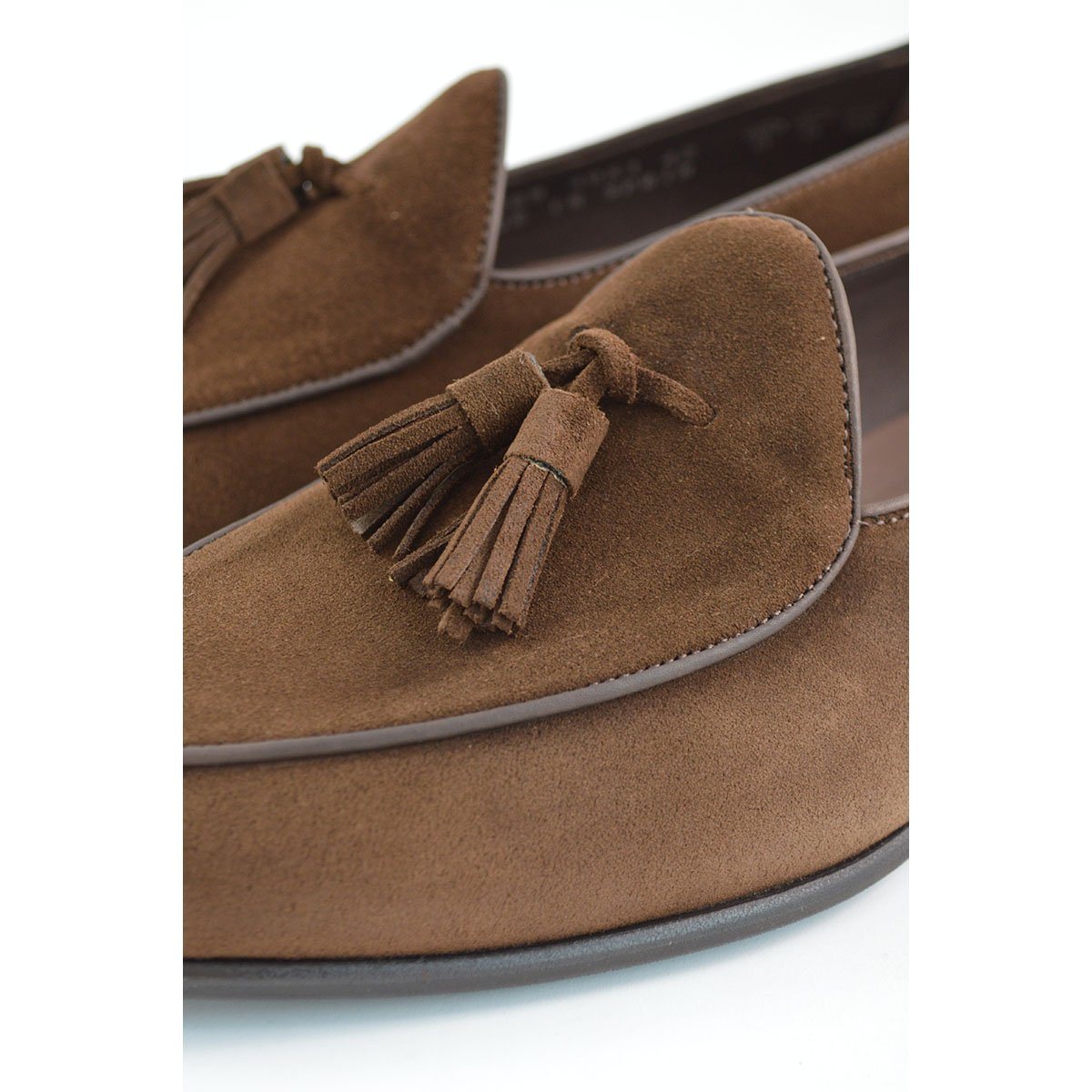 A dark brown suede tassel loafer with a Vegano Moka leather trim, displaying an almond-shaped toe and a fine ridged rubber sole.