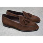 A dark brown suede tassel loafer with a Vegano Moka leather trim, displaying an almond-shaped toe and a fine ridged rubber sole.