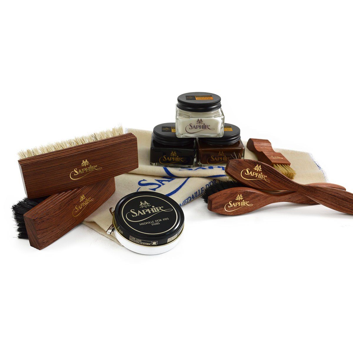 An assortment of shoe care products from Saphir Medaille D'Or including polishing cloths, brushes, cream polishes in black and medium brown, a shoe bag and a neutral wax polish.