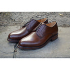 A dark brown, grainy-textured leather derby shoe with a round toe and classic lace-up closure & Dainite soles