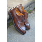 A pair of dark brown Berwick 1707 Split Toe Derby shoes with laces, set against a sandstone step background