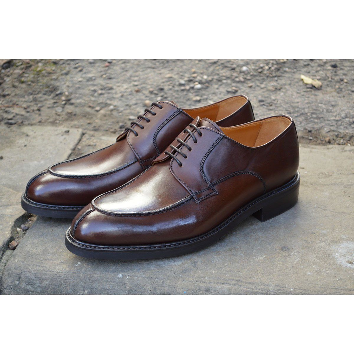 A pair of dark brown Berwick 1707 Split Toe Derby shoes with laces, set against a sandstone step background