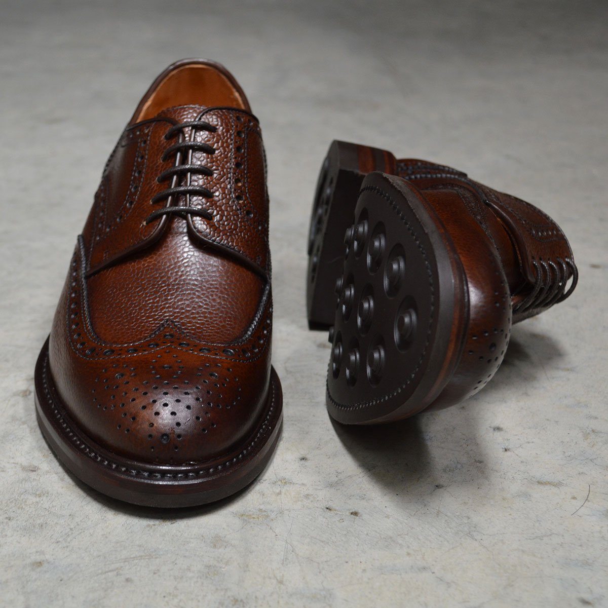 A Berwick 1707 brown brogue derby shoe with a round toe shape and lace-up closure. It features a grainy texture and brogue detailing & Dainite soles