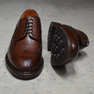 A Berwick 1707 brown brogue derby shoe with a round toe shape and lace-up closure. It features a grainy texture and brogue detailing & Dainite soles