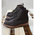 A dark brown Trickers Bernwood service boot made of Hydro Nubuck with a Dainite sole, featuring brass eyelets and a cream Barbour welt.